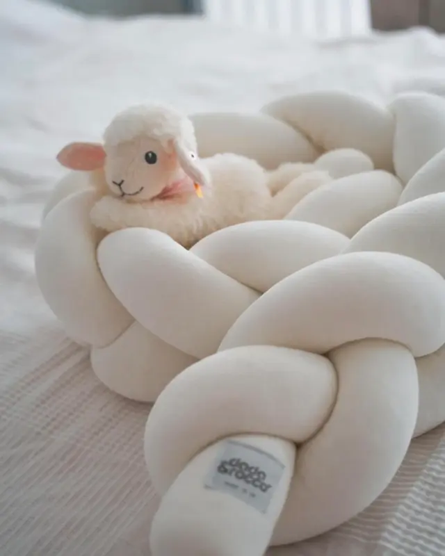 Small plush sheep nestled among smooth white pebbles in a soft, bright setting.