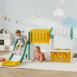 Two young children play on a bright plastic slide in a pastel playroom with cloud and star wall decor.