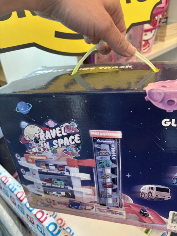 Child’s hand threads a yellow flexible tube into a space-themed toy box labeled Travel in Space