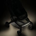 Low-angle view of a sleek black stroller with an illuminated front bumper on a dark background.