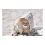 Baby in a striped hooded robe lying on sandy beach with a pacifier in mouth.