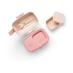 Pastel pink bento-style lunchbox with a beige inner tray and a matching small beige container, plus a pink utensil set nearby.