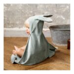 Baby seated on a wooden floor wearing a gray hooded towel with bunny ears as a cape.