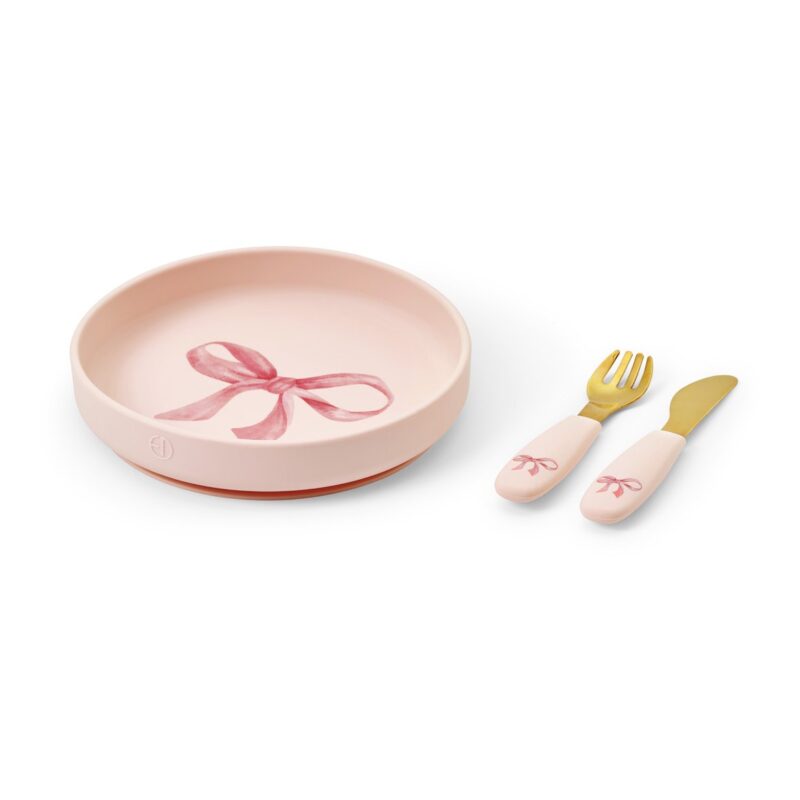 Pastel pink children's dish set: round bowl with bow design and matching pink-handled spoon and fork with gold tips.