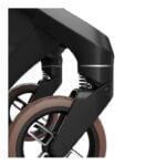 Close-up of a black folding frame with a sprung front wheel and brown tire, highlighting the suspension joints.