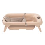 Peach-colored portable baby bassinet with padded liner, safety straps, and foldable legs.