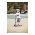 Young child wearing a blue helmet and knee pads rides a blue scooter outdoors on a sunny day.