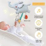Baby in a white outfit reaches for a soft hanging elephant mobile with attached toys above a bassinet, designed to entertain and soothe.