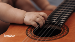 Close-up of a baby's hand resting on the strings and fretboard of an acoustic guitar