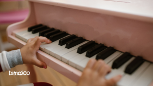 Close-up of a child's hands playing a pink upright piano, focusing on the black and white keys.