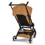 Stroller with tan fabric and black frame, four wheels, and a storage basket beneath the seat.