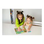 Two young girls with pigtails sit at a white table, placing pieces in a colorful animal puzzle together.