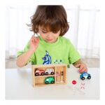 Young child in a lime-green shirt plays with a wooden toy garage and vehicles on a table in a bright room.