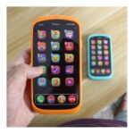 Hand holding an orange-protected phone showing colorful app icons; a blue phone on a wooden table in background.