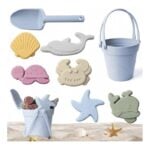 Beach sand toy set: blue shovel, bucket, shell, turtle, crab and starfish molds on sand with seashells nearby.