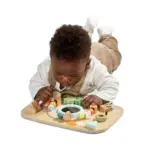 Infant on their stomach playing with a colorful wooden activity board and shapes.