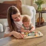 Mother and baby playing with a wooden sensory activity board on a coffee table in a cozy living room