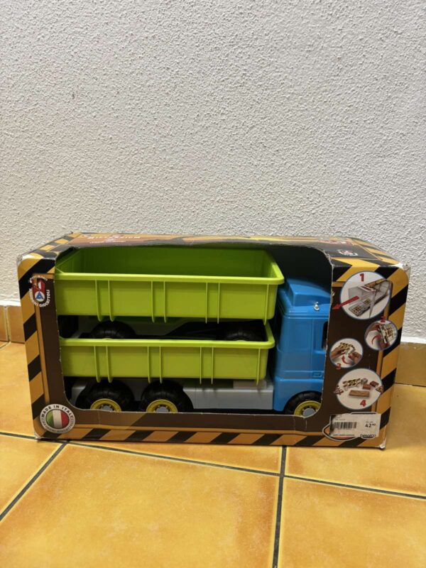 Toy truck with two lime-green cargo containers stacked in a blue cab, packaged in a cardboard box against a wall.
