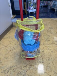 Clear tote bag attached to a red shopping cart, showing a blue water bottle inside, in a store aisle with yellow trim on the bag handles.