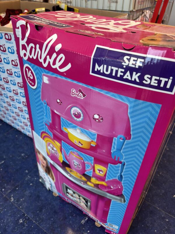 Pink Barbie kitchen playset box with a pretend stove, pots, and utensils; Turkish text 'Şef Mutfağı Seti' visible on the packaging; bright blue accents and chef-themed graphics show it's a kids' toy.
