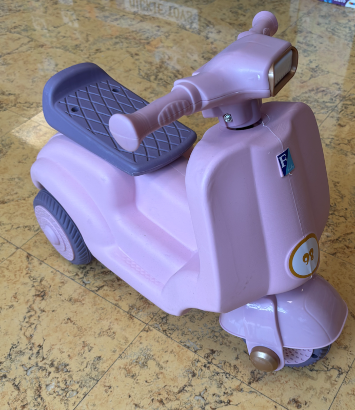 Pink plastic kids’ ride-on scooter with a gray footboard on a tiled floor.