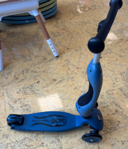 Blue kids' kick scooter with a textured deck and two small rear wheels on a beige tile floor.