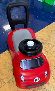 Red Smoby kid's ride-on toy car with gray seat and black steering wheel, displayed indoors on a yellow floor."