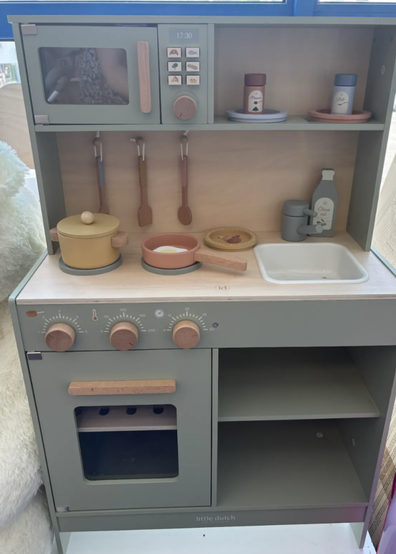 Wooden toy kitchen with stove, oven, sink, and utensils in muted gray and pastel colors.